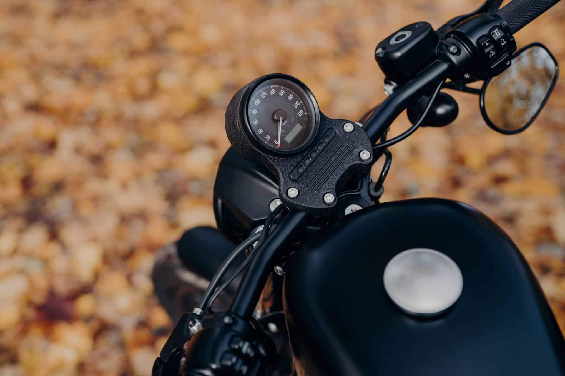 Nahaufnahme eines Motorrad-Tachos mit buntem Herbstlaub im Hintergrund; vermittelt Fahrgefühl, Präzision und den passenden Einsatz von Shoei Helmen.