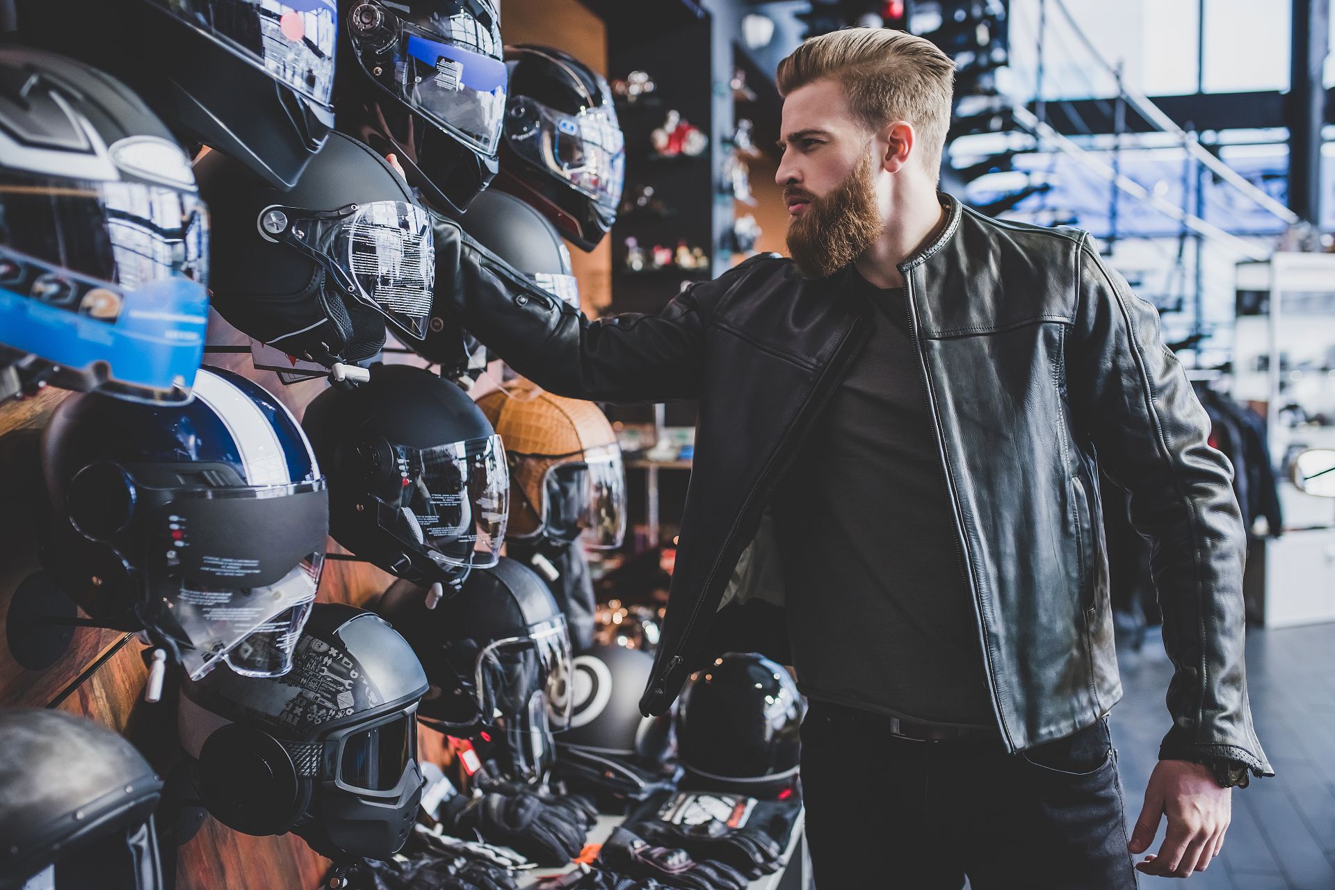 Mann mit Lederjacke betrachtet verschiedene Motorradhelme im Geschäft; symbolisiert Auswahl, Sicherheit und Kaufentscheidung für Shoei Helme.